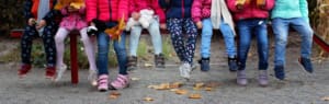 eight children's legs lined up on bench wearing colourful shoes and trousers